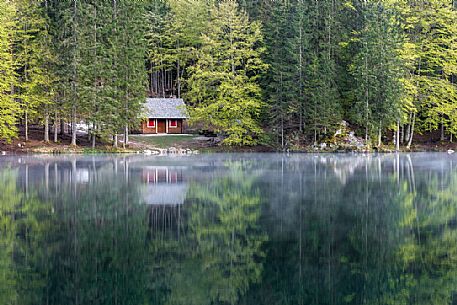 A small house reflects on the beautiful waters of the lower lake of Fusine, Tarvisio, Julian Alps, Friuli Venezia Giulia, Italy, Europe